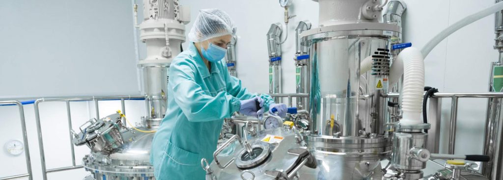 ravailleuse d'usine pharmaceutique dans des vêtements de protection opérant la ligne de production dans un environnement stérile